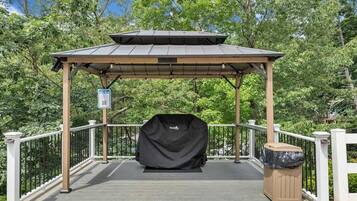 A covered outdoor area with a pergola, a barbecue grill, and a trash bin.