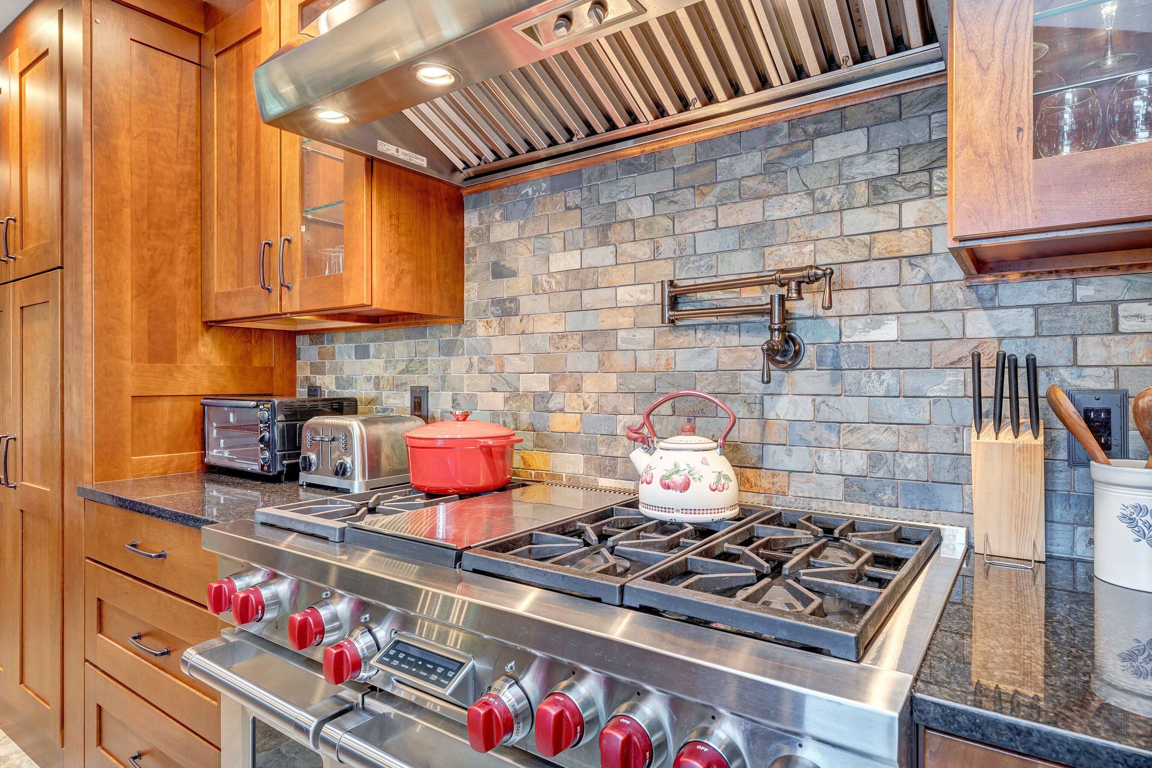 A kitchen with wooden cabinets, a gas stove, a red pot, a kettle, and a toaster.