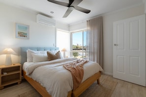 A bedroom with a bed, bedside lamps, a ceiling fan, a window with curtains, and a door.