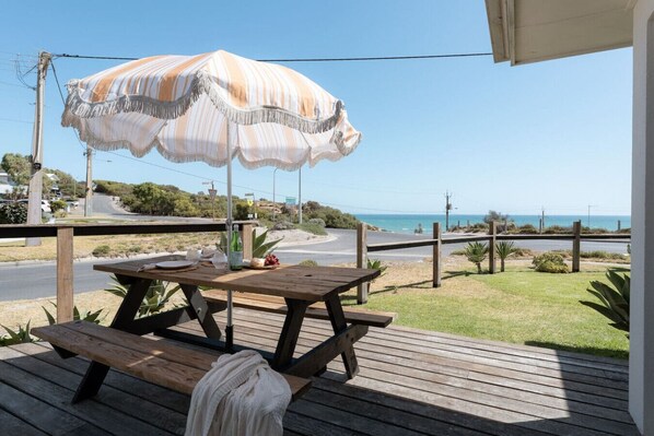 A wooden deck with a picnic table and an umbrella, overlooking a coastal road and ocean. - The Nook Studio ~ 1 bedroom ~ stunning ocean views (Aldinga Beach)