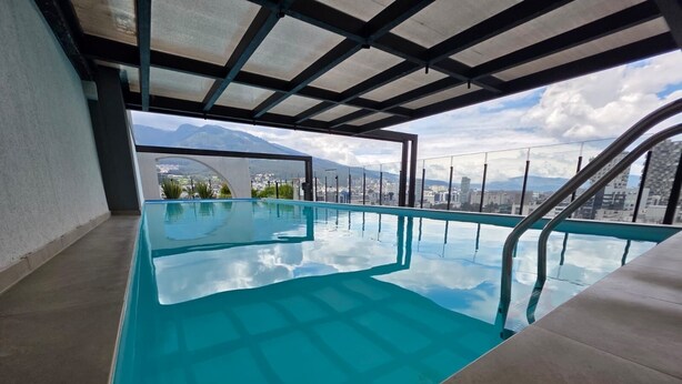 An indoor swimming pool with a clear view of a cityscape and mountains in the background. - Luxury Studio in Harmony - Best Area Quito, Pool, Gym & Fast WiFi (Quito)