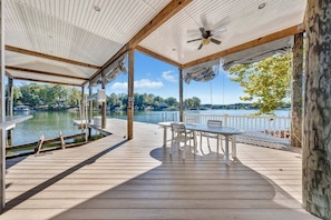 A covered deck with a table and chairs, overlooking a lake with a dock and boats. - Lake Paradiso - Lakefront Home With Private Dock (Moneta)
