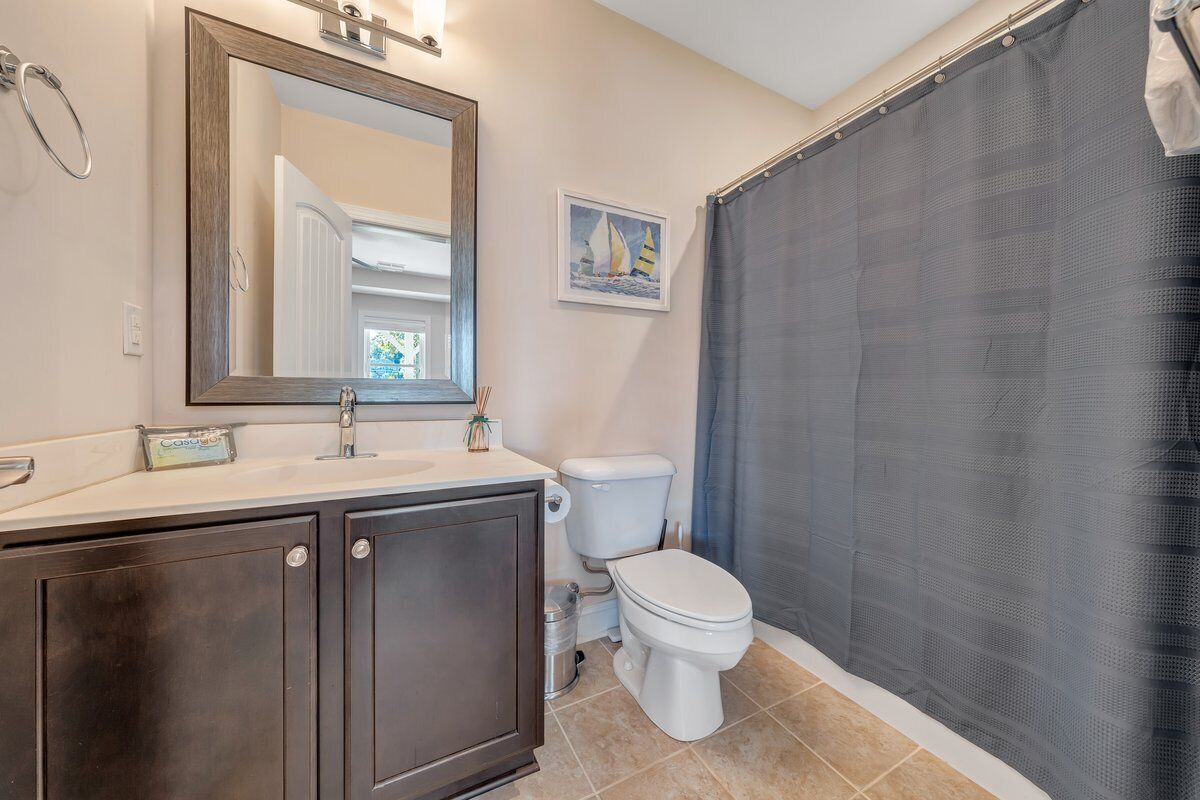 A bathroom with a dark wooden vanity, a white toilet, a large mirror, and a shower curtain.