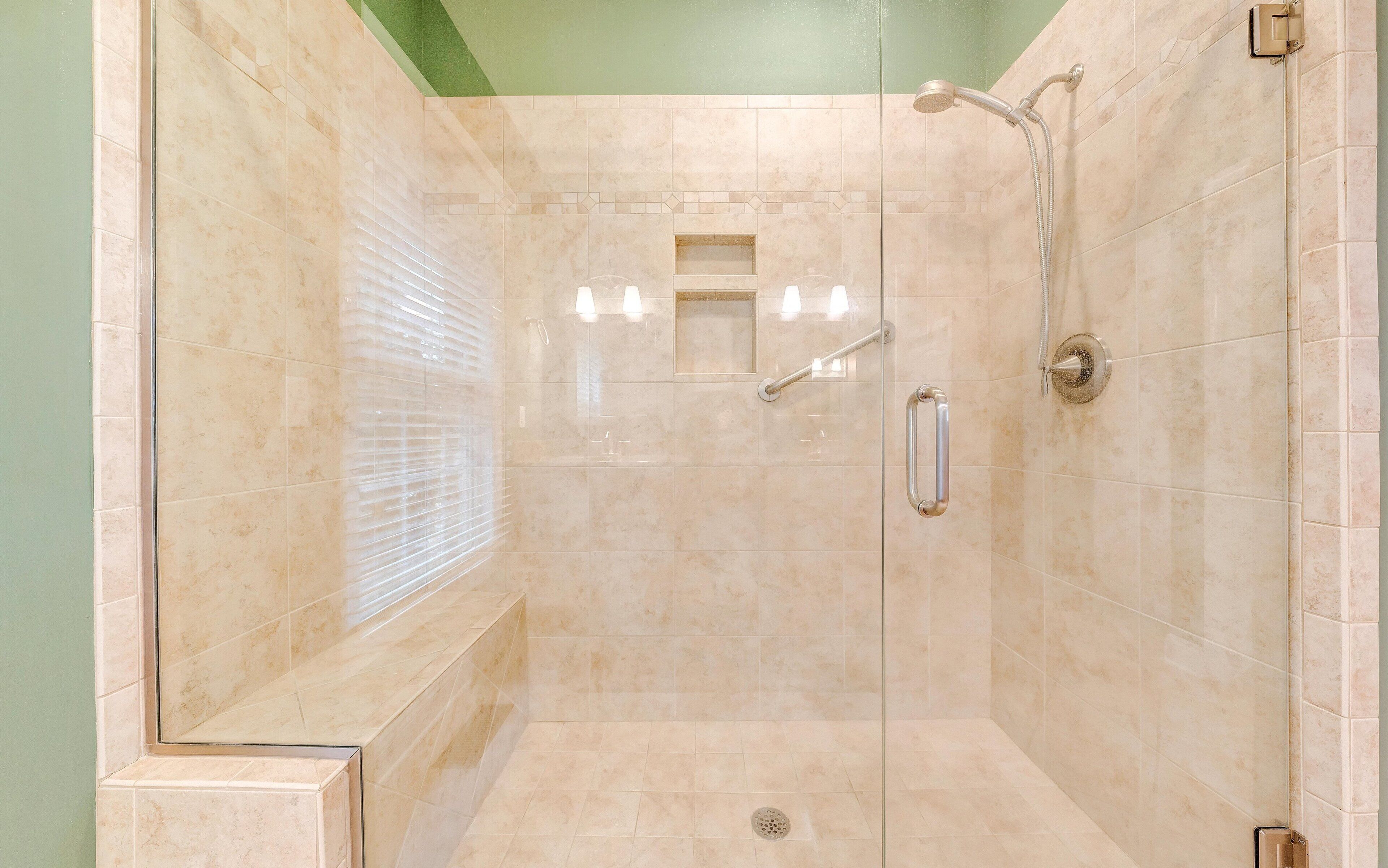 Eine begehbare Dusche mit beigen Fliesen, einer Handbrause und einer Glaswand.