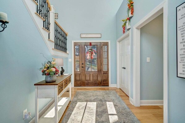 A hallway with a wooden door, a white console table with a vase of flowers, and a gray rug. - Serenity Shores - Private Lakefront Home With Dock (Moneta)