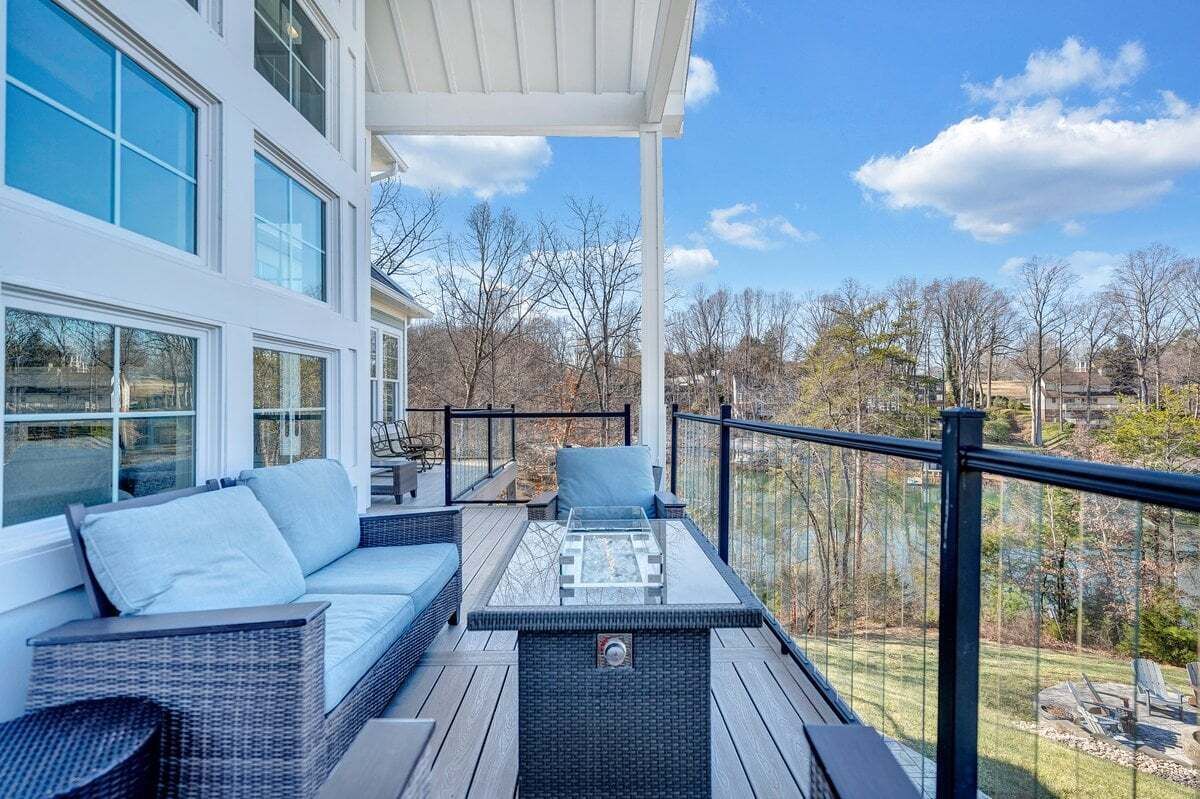 A modern outdoor deck with a sofa, a glass-top table, and a railing.