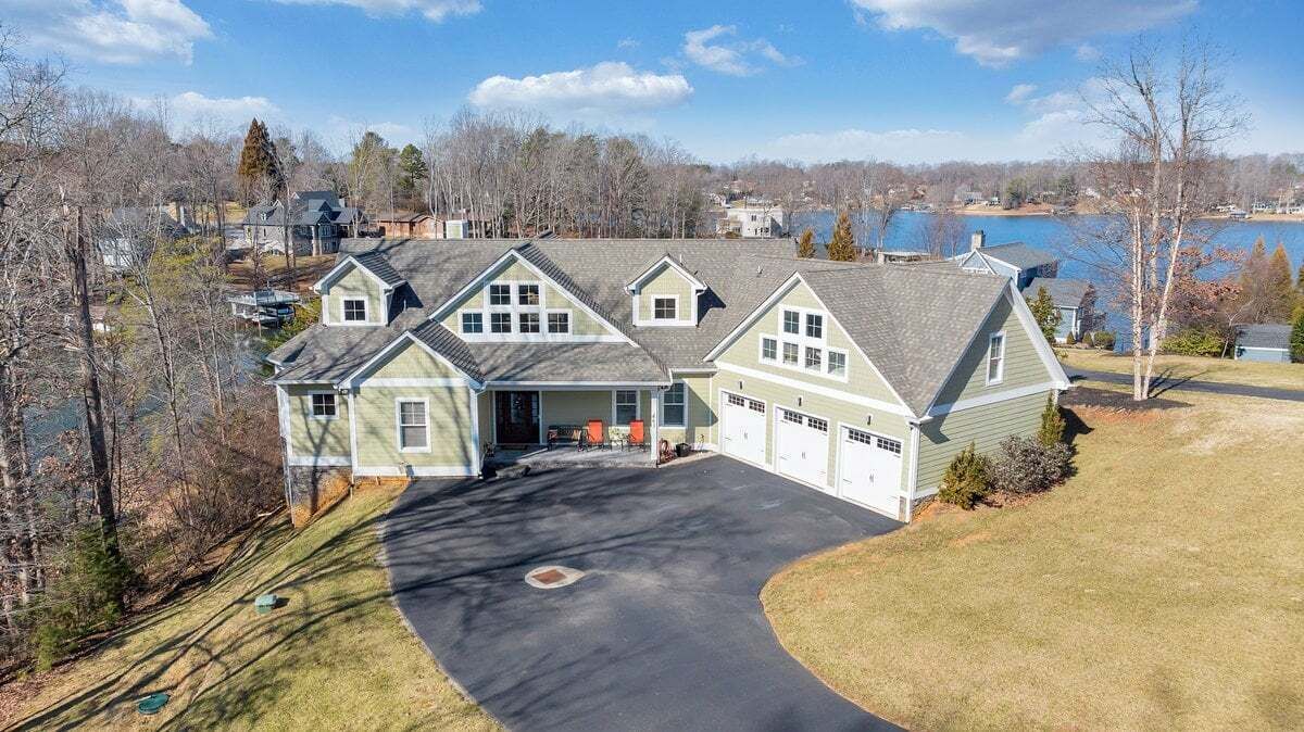 A large, two-story house with a garage, a driveway, and a lake in the background.