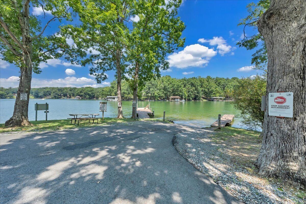 A lakeside picnic area with a bench, picnic table, and a sign prohibiting aquatic hitchhiking.
