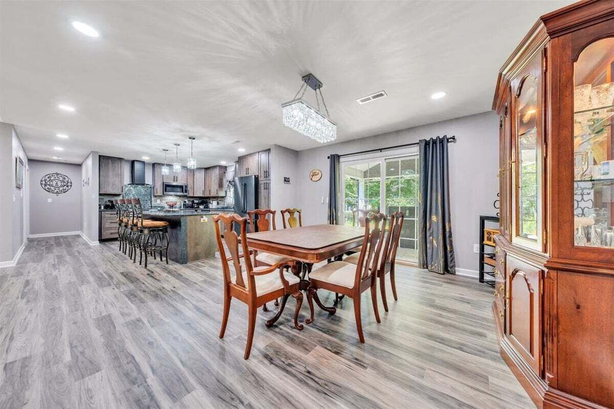 A spacious dining area with a wooden table and chairs, a kitchen in the background, and a large wooden cabinet with glass doors.