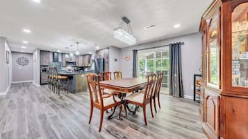 A spacious dining area with a wooden table and chairs, a kitchen in the background, and a large wooden cabinet with glass doors.