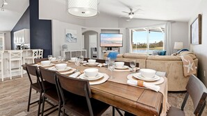 A modern dining area with a wooden table set for six, a sofa, and a television in the background. - Golden Pond Lakehouse. Tranquil lake retreat with charm, designer style & private pool by Disney (Kissimmee)