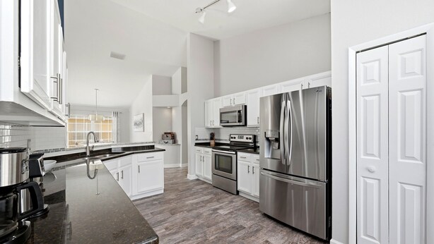 A modern kitchen with white cabinets, stainless steel appliances, and a dark granite countertop. - Golden Pond Lakehouse. Tranquil lake retreat with charm, designer style & private pool by Disney (Kissimmee)