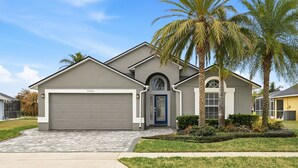 A modern two-story house with a garage, a blue front door, and a well-maintained lawn with palm trees. - Golden Pond Lakehouse. Tranquil lake retreat with charm, designer style & private pool by Disney (Kissimmee)