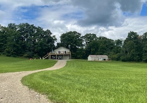 Een groot grasveld met een grindpad dat naar een huis met een veranda leidt.