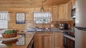 Une cuisine de style rustique, avec des éléments en bois, un îlot central, des appareils en acier inoxydable et une fenêtre agrémentée d’un rideau à motifs.