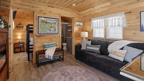 L’intérieur d’un chalet accueillant, avec un plafond en bois, un canapé de couleur sombre agrémenté de coussins sur le thème du voyage, une carte accrochée au mur et un petit tapis.