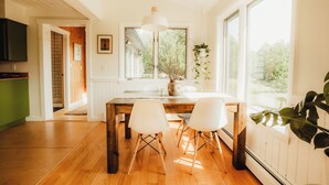 Una cocina luminosa con piso de madera, sillas blancas, una mesa de madera y ventanas amplias.