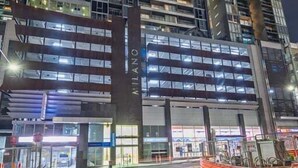 A high-rise building with multiple floors, large windows, and a prominent entrance area with visible signage. - Convenient CBD Retreat in the Best Location! 2 Bed | 2 Bath | 2 Parking (Melbourne)