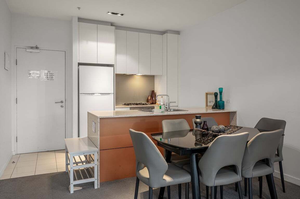A compact kitchen with white cabinets, a small dining area with four chairs, and a single table.