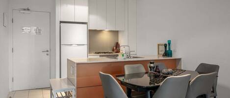 A compact kitchen with white cabinets, a small dining area with four chairs, and a single table.