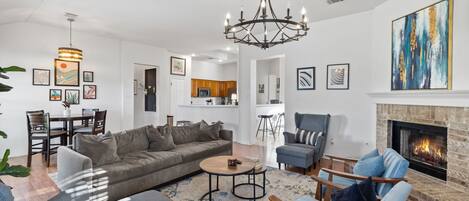 A modern living room with a fireplace, a dining area, and a kitchen in the background.