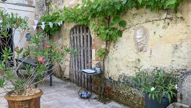 Une terrasse extérieure agrémentée d’un mur en pierre rustique, d’une porte en bois et de divers pots de plantes.
