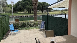 A patio with a table and chairs, a palm tree, and a view of a park with a pond. - Pleasant studio cabin apartment in residence with pool near Richelieu beach, Cap d'Agde (LE CAP D AGDE)