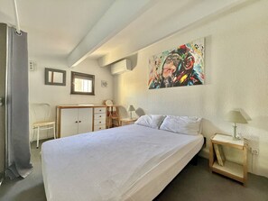 Une chambre à coucher avec un lit, un bureau, une chaise, une fenêtre et un tableau accroché au mur.