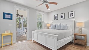 Una camera da letto con un letto bianco, una ventola a soffitto, un comodino in legno e un tavolino.