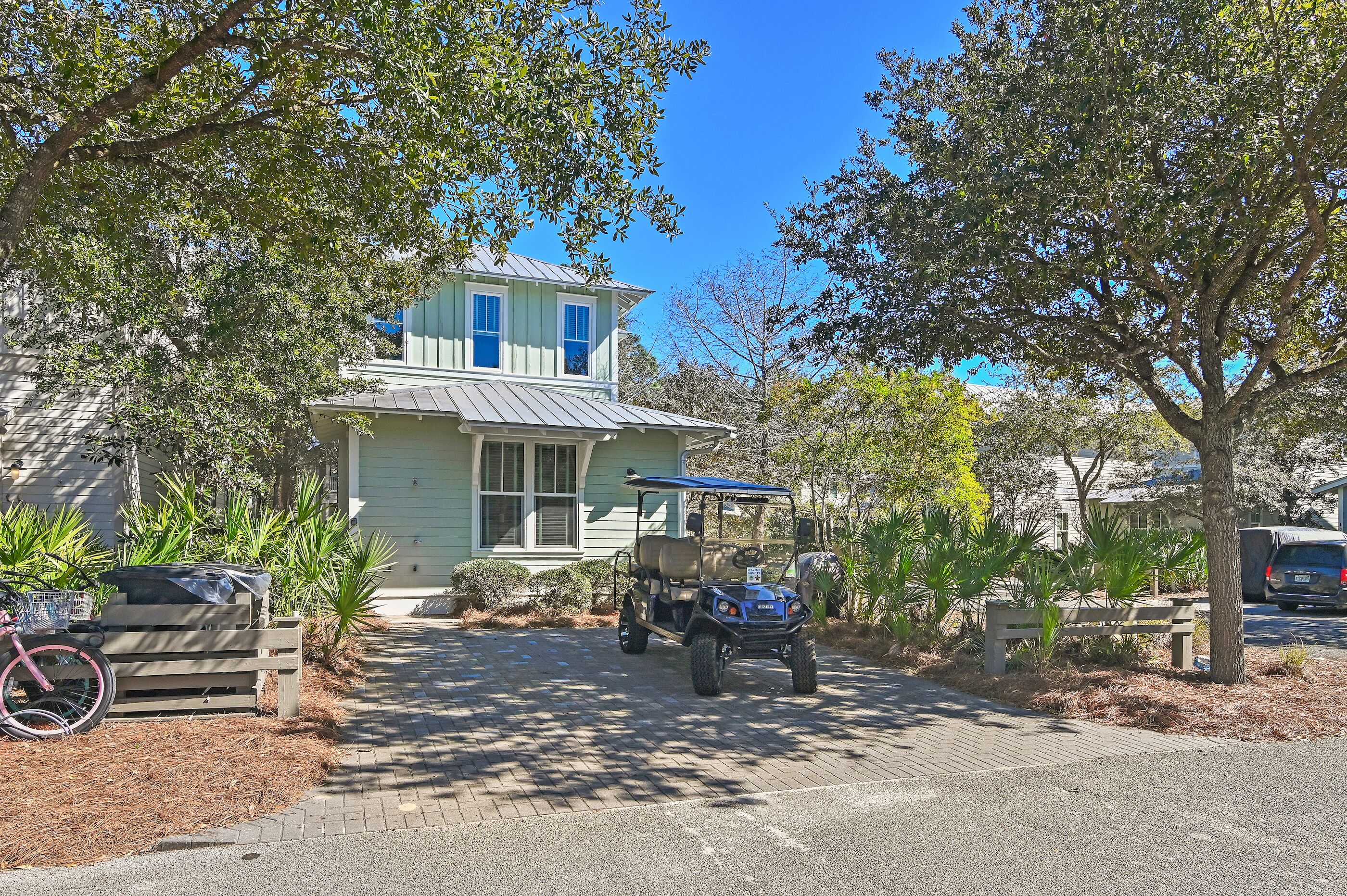 A two-story house with a garage, a parked golf cart, and a bicycle leaning against a bench.