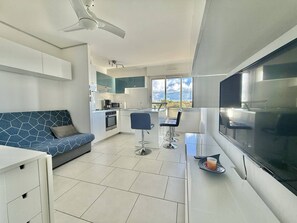 A modern kitchen with white cabinets, a blue sofa, and a dining area with two bar stools. - CAP D'AGDE - Les Falaises / Réf 146 (CAP D'AGDE)
