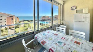Un balcón con vista al mar y edificios, un refrigerador blanco, un microondas y una cama con colcha colorida.