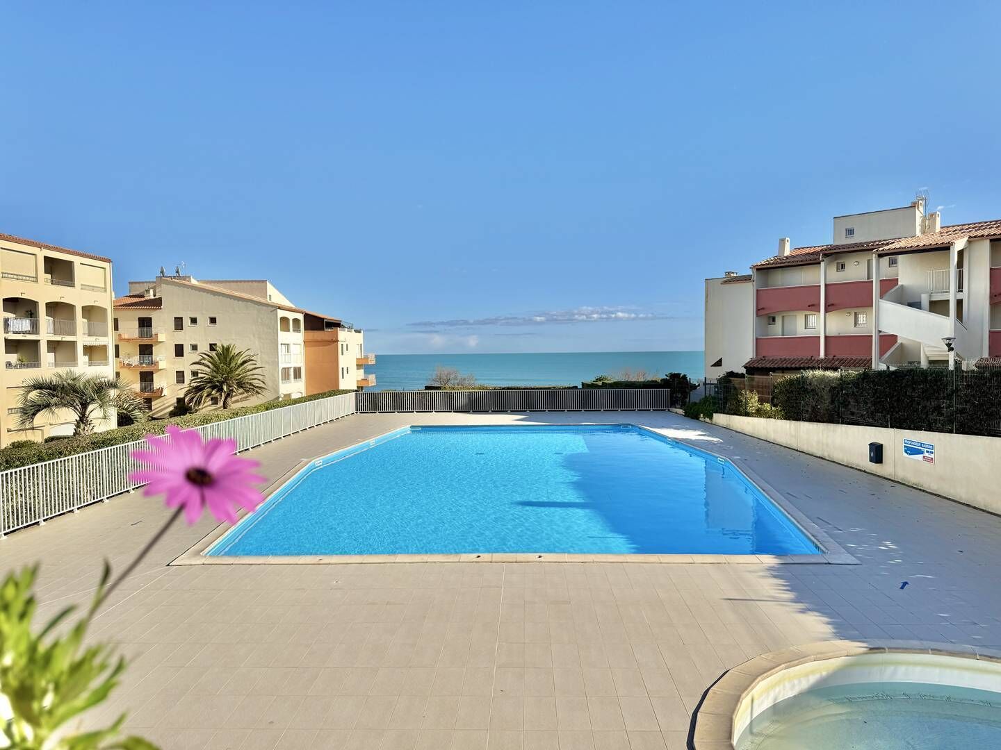 A swimming pool with a view of the sea, surrounded by apartment buildings.