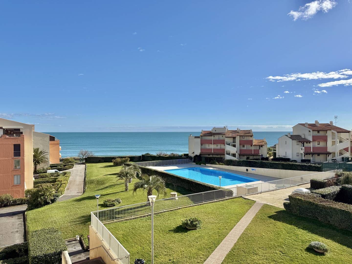 A residential area with a swimming pool, a view of the sea, and a well-maintained lawn.