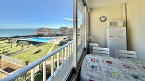 Un balcón con vista a la piscina, una cama con cubrecama estampado, un microondas y un refrigerador.