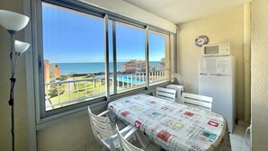 Un balcón con mesa y sillas, vista al mar y un microondas en la pared.