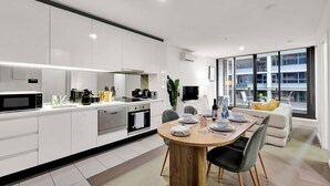 Een moderne keuken met witte kasten, een eethoek met een houten tafel en een groot raam met uitzicht op de stad.