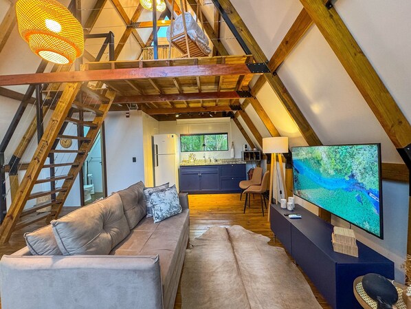 Un dormitorio en el ático con cama tipo loft, un sofá, un televisor y una zona de cocina.
