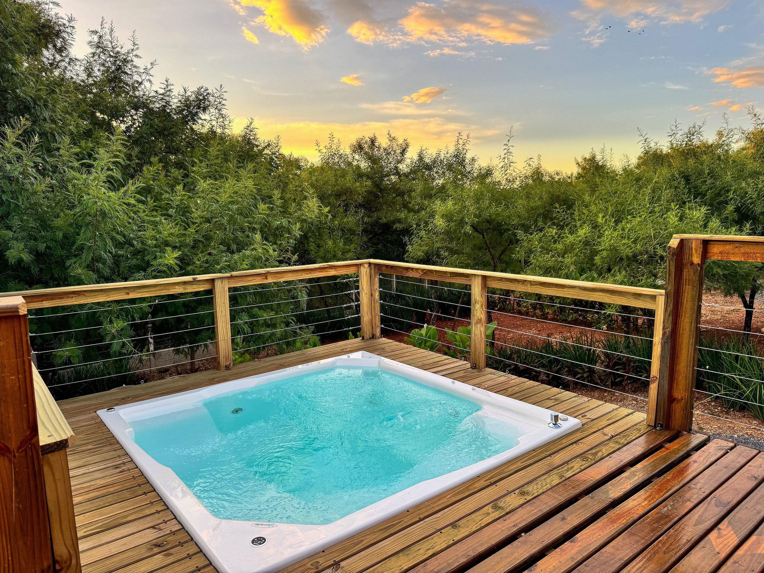 A hot tub on a wooden deck with a wooden railing and a view of trees.