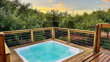 A hot tub on a wooden deck with a wooden railing and a view of trees.