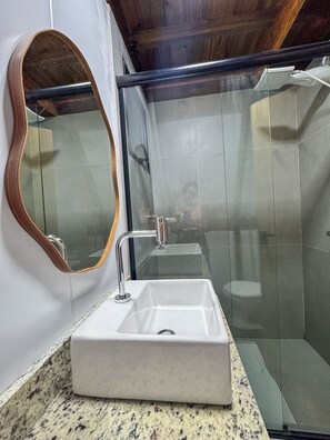 Une salle de bain avec un lavabo rectangulaire, un miroir et un espace douche.