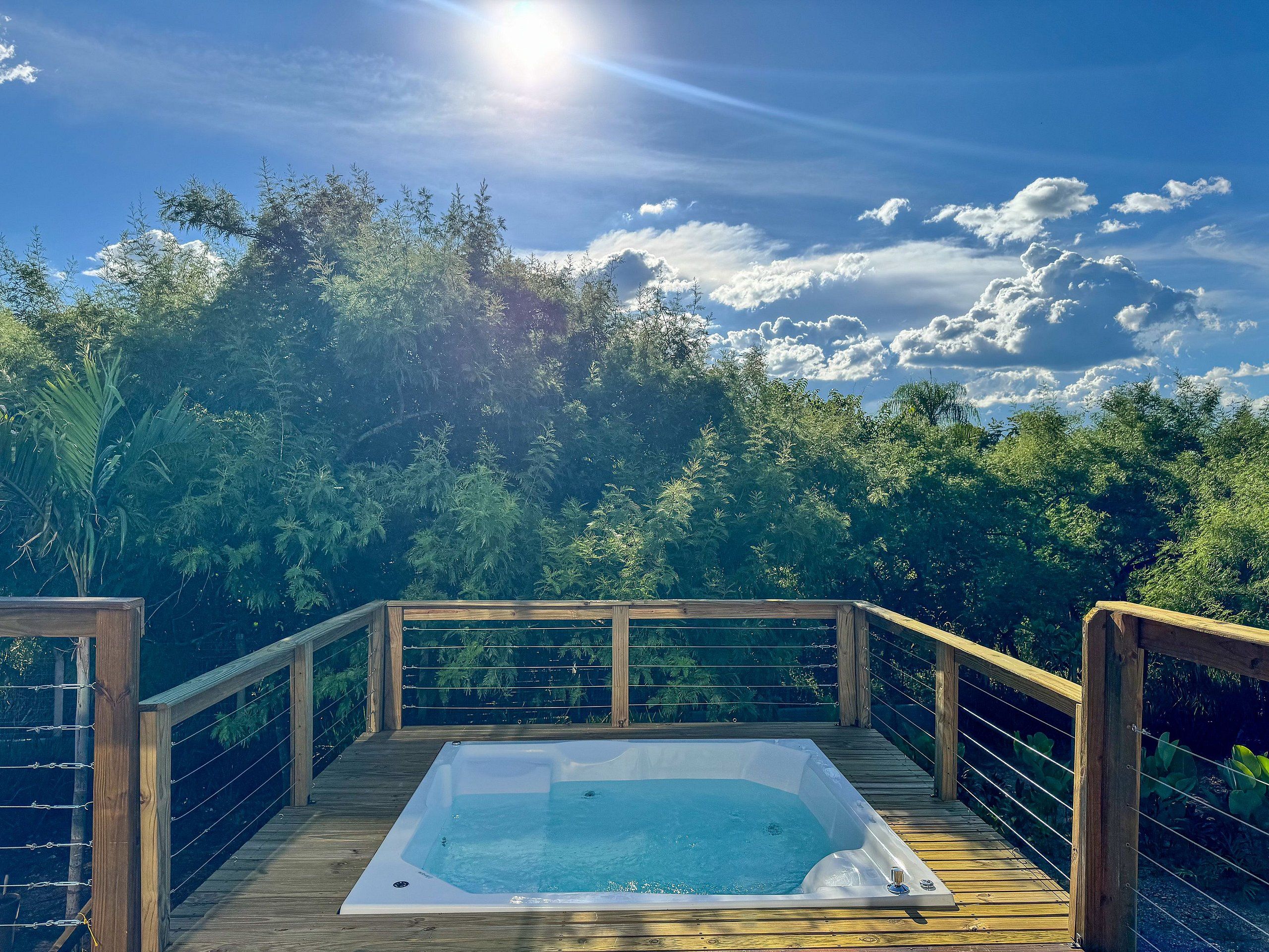 A hot tub on a wooden deck with a view of dense greenery and a clear sky.