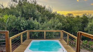 A wooden deck with a hot tub surrounded by dense foliage.
