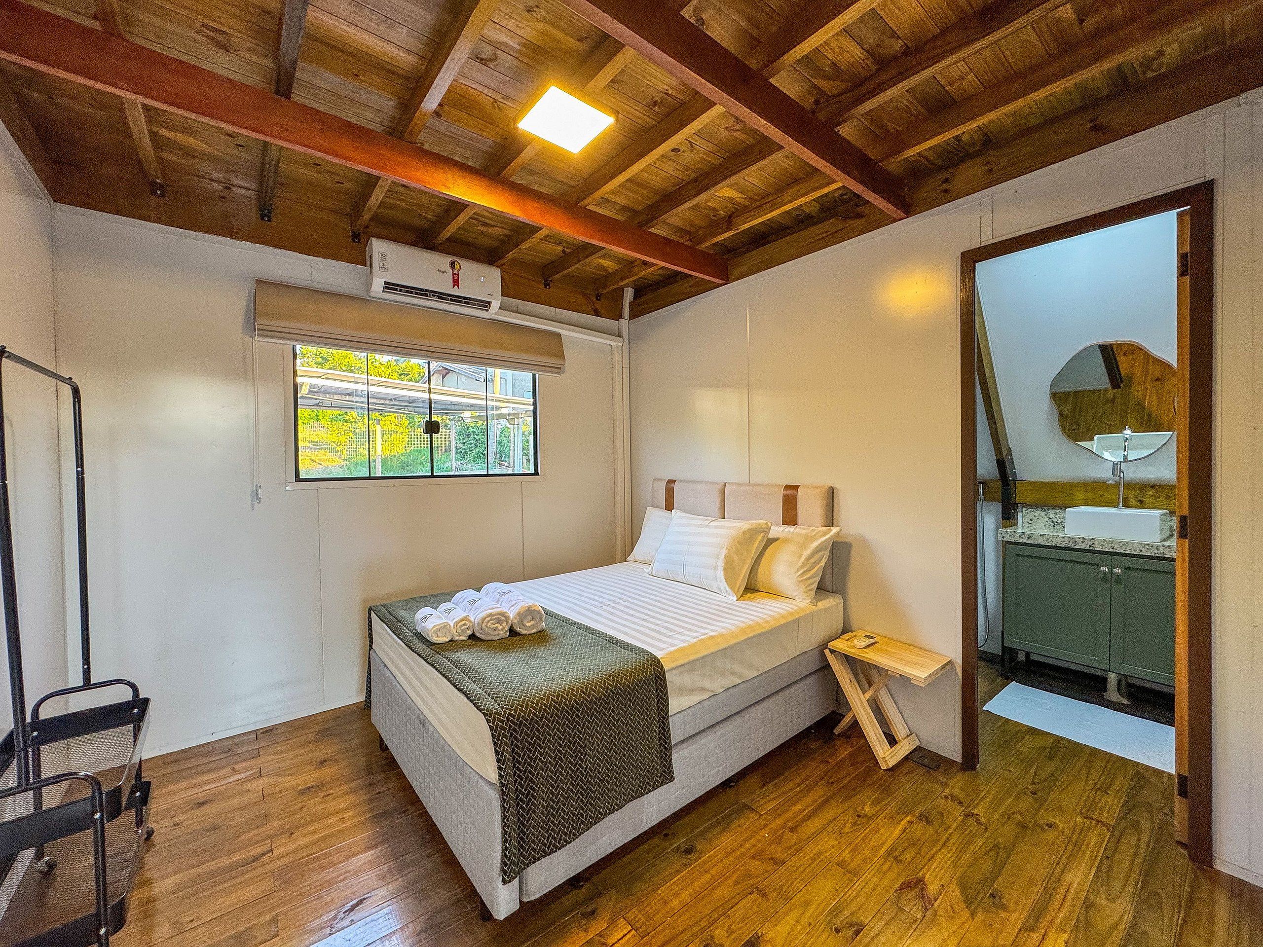 Quarto com cama, janela, aparelho de ar condicionado, espelho e teto de madeira.