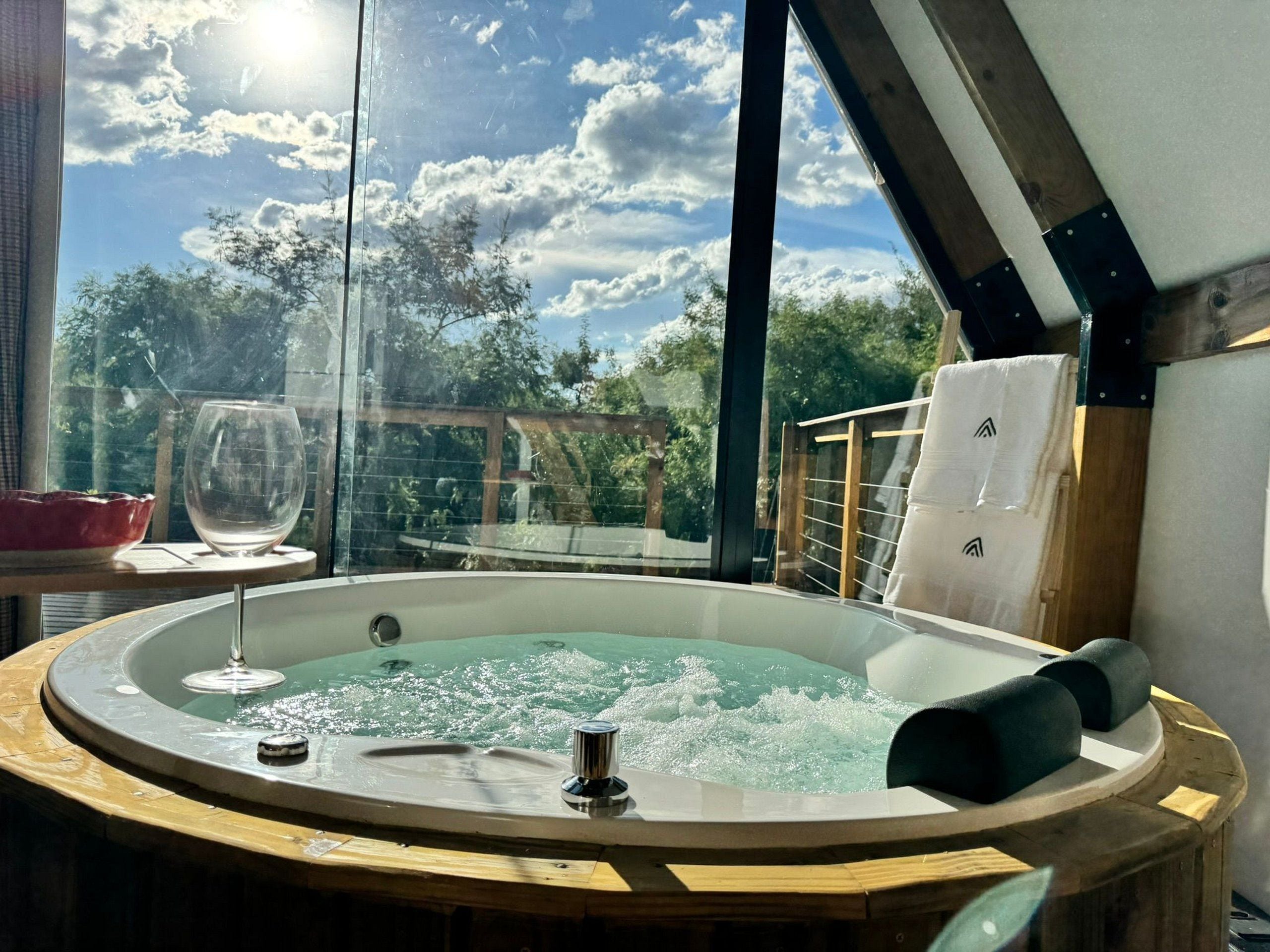 A hot tub with a glass enclosure, a glass wine glass, and a wooden deck with a railing.