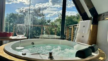 A hot tub with a glass enclosure, a glass wine glass, and a wooden deck with a railing.
