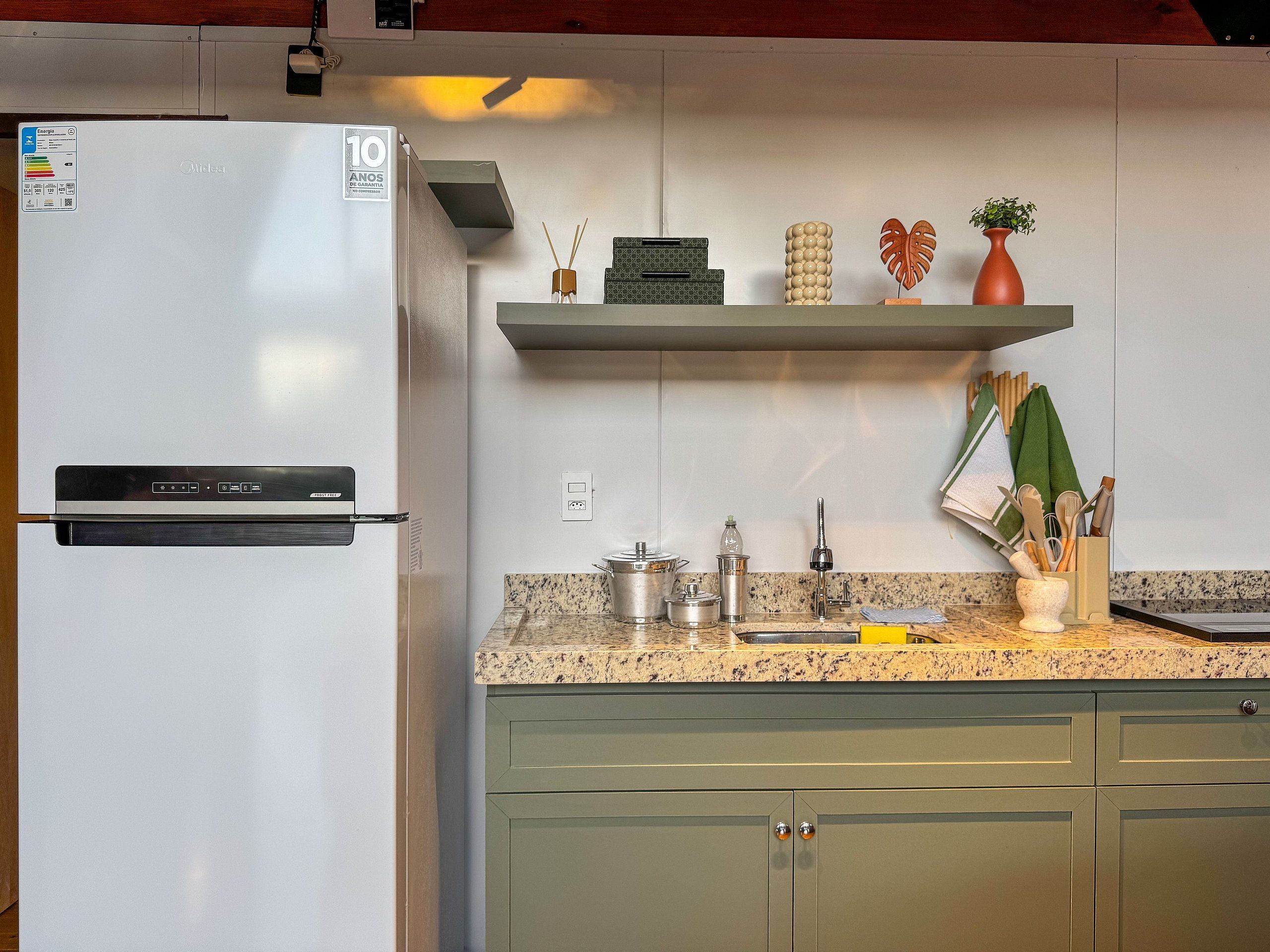A kitchen with a white refrigerator, granite countertop, green cabinets, and various kitchen items on the shelves.
