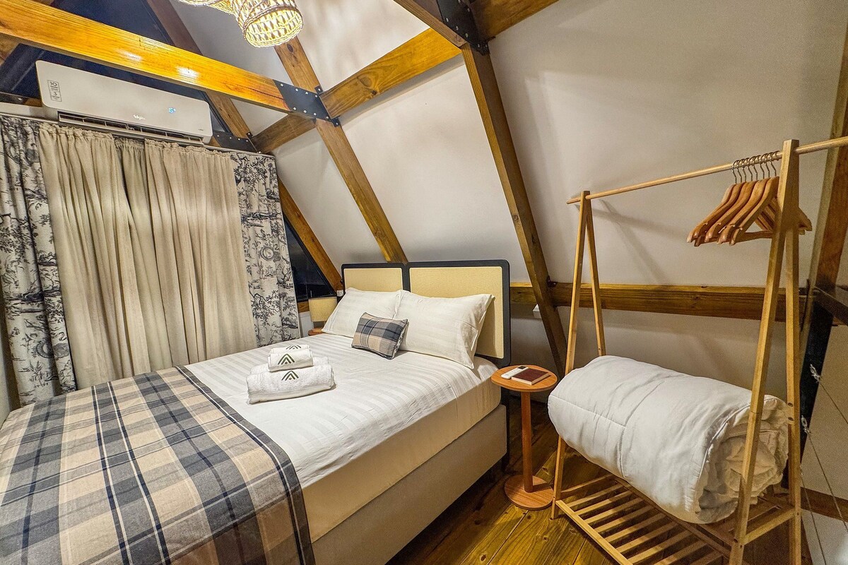Ein Schlafzimmer mit einem Bett, einer Kleiderstange, einem Nachttisch und einem Fenster mit Vorhängen.