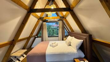 A triangular room with a bed, wooden beams, a window with curtains, and a hanging light fixture.