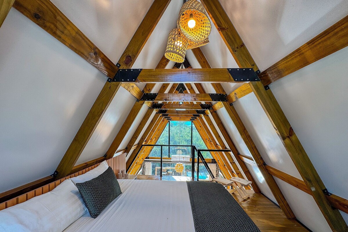Ein Schlafzimmer im Dachgeschoss mit einem Bett, zwei Kissen, einer Hängeleuchte und Blick ins Freie.